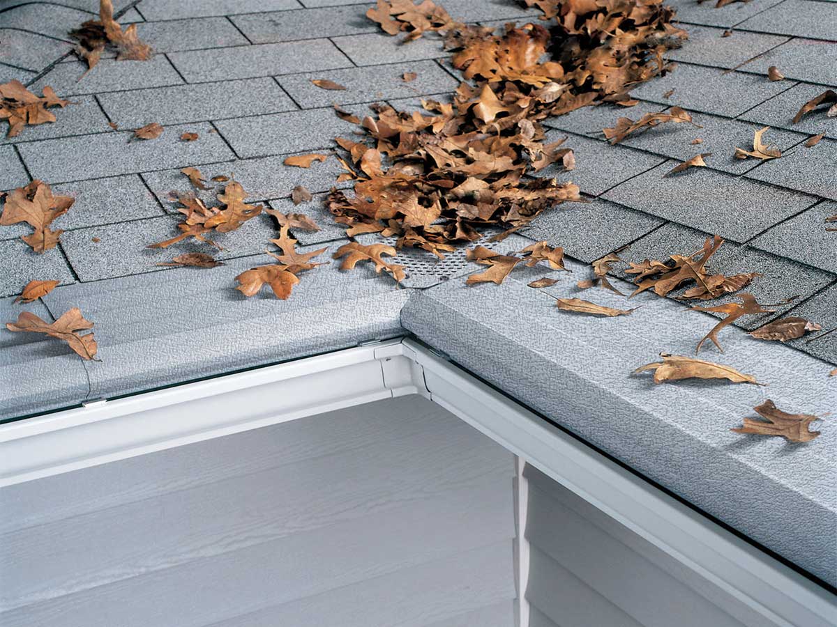 Dry oak leaves resting on top of a Gutter Helmet cover at a roof corner, kept out of the gutter beneath
