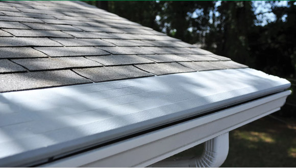Gutter Helmet cover installed along the edge of a shingled roof, shielding the gutter below
