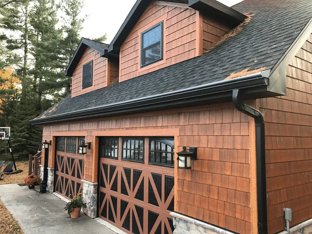 Black Gutter Helmet installed along the front of a cedar shake garage