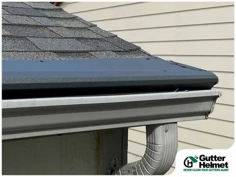 Dark gray Gutter Helmet cover installed over a gutter on a shingle roof